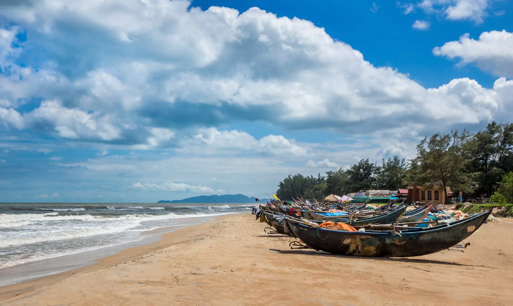 A row of fishing boats on golden sands of a beach.