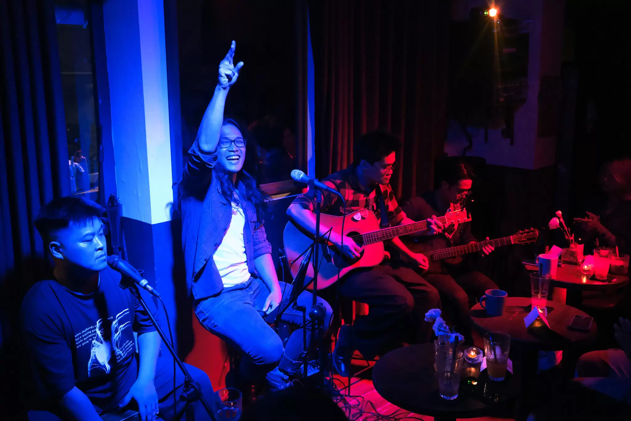 A band performs in a dark, intimate space under blue and red lighting