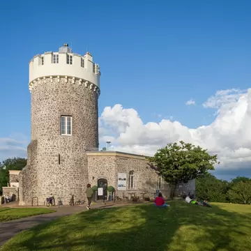 Round stone tower with a white crenellated top on a grassy hilltop in Bristol, people relaxing on the lawn