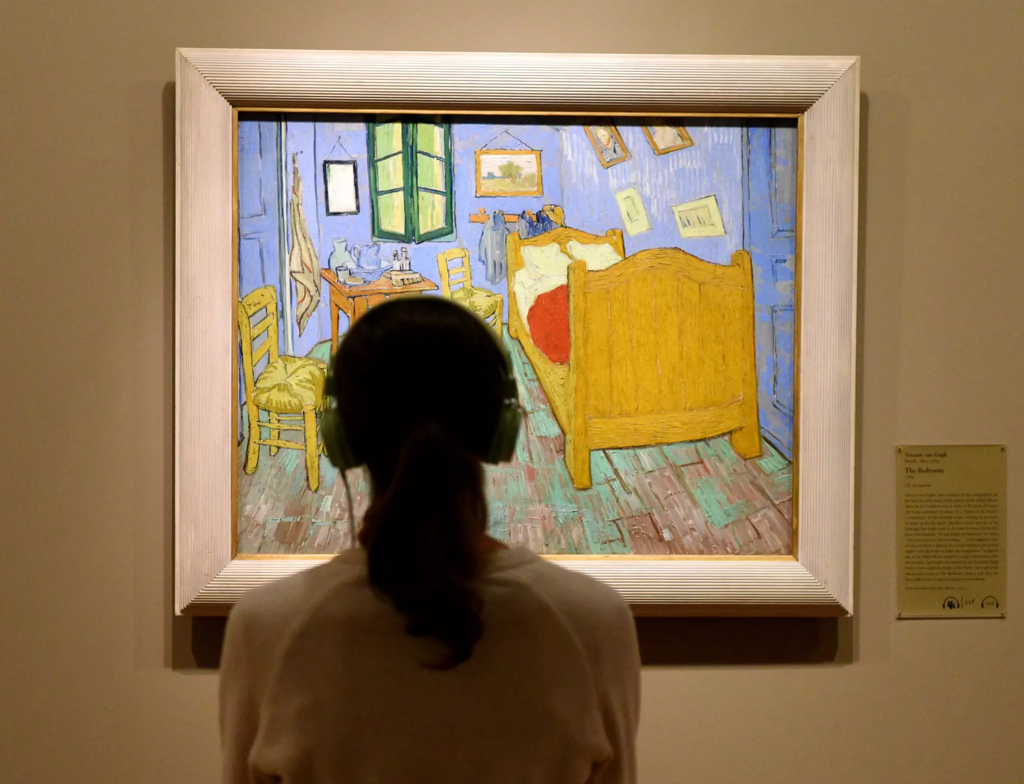 A woman wearing headphones looks at the ”The Bedroom” by Vincent van Gogh – depicting a bed and chairs in a small room – at the Art Institute of Chicago.