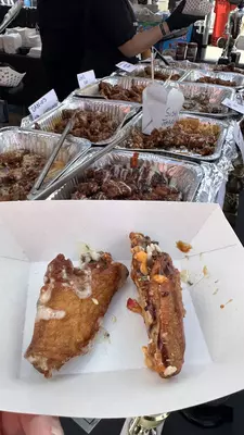 Aluminum trays of chicken wings in various sauces with tongs ready to be served