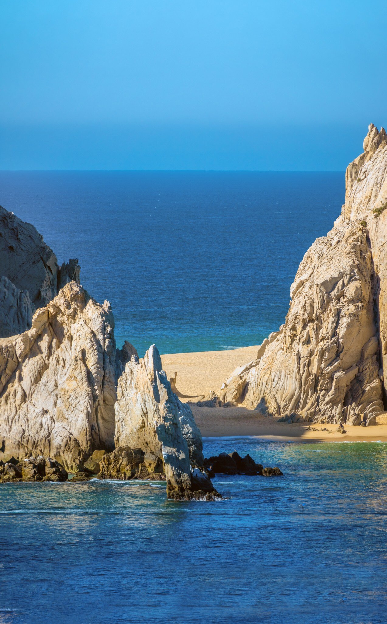 A strip of golden sand between large rock formations with blue water on either side.