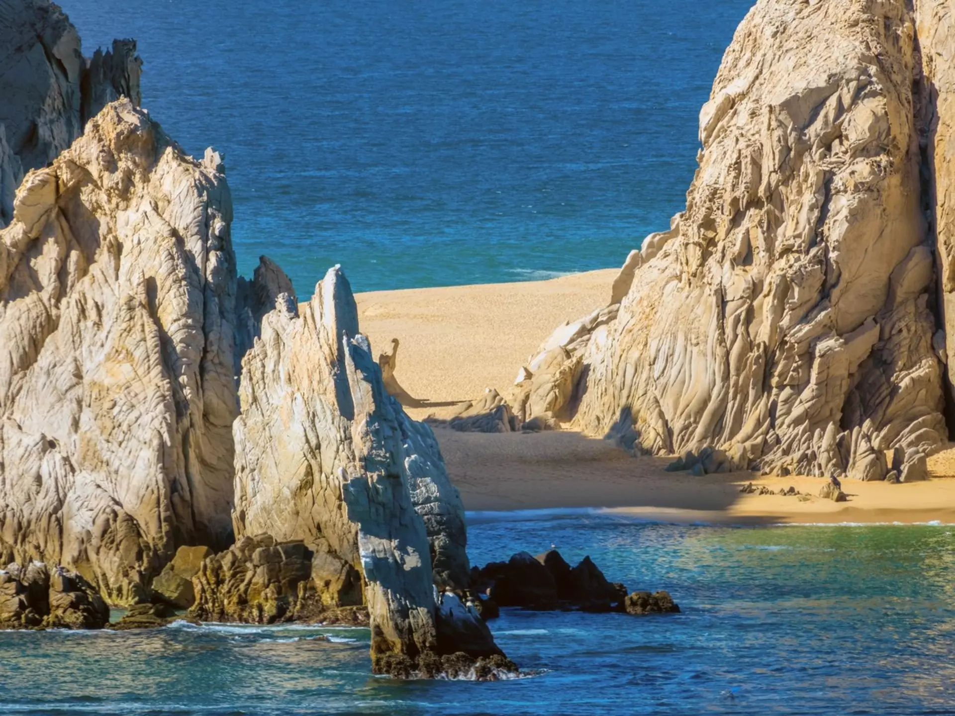 A strip of golden sand between large rock formations with blue water on either side.