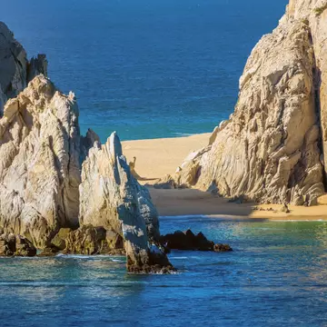 A strip of golden sand between large rock formations with blue water on either side.