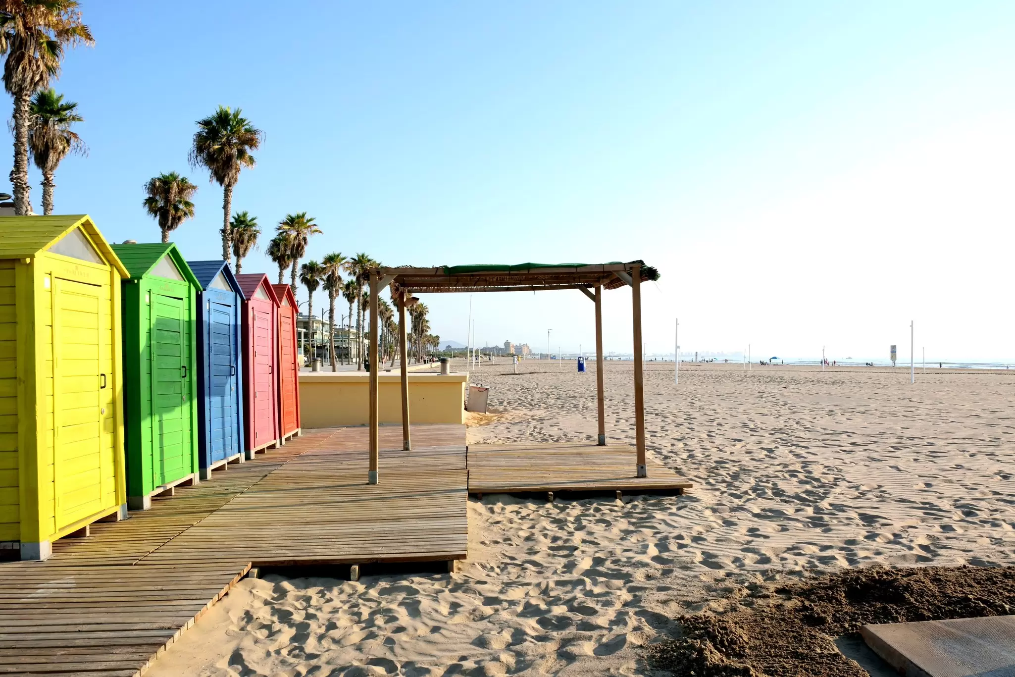 Brightly painted wooden cabins beside a sandy beach, lined with palm trees.