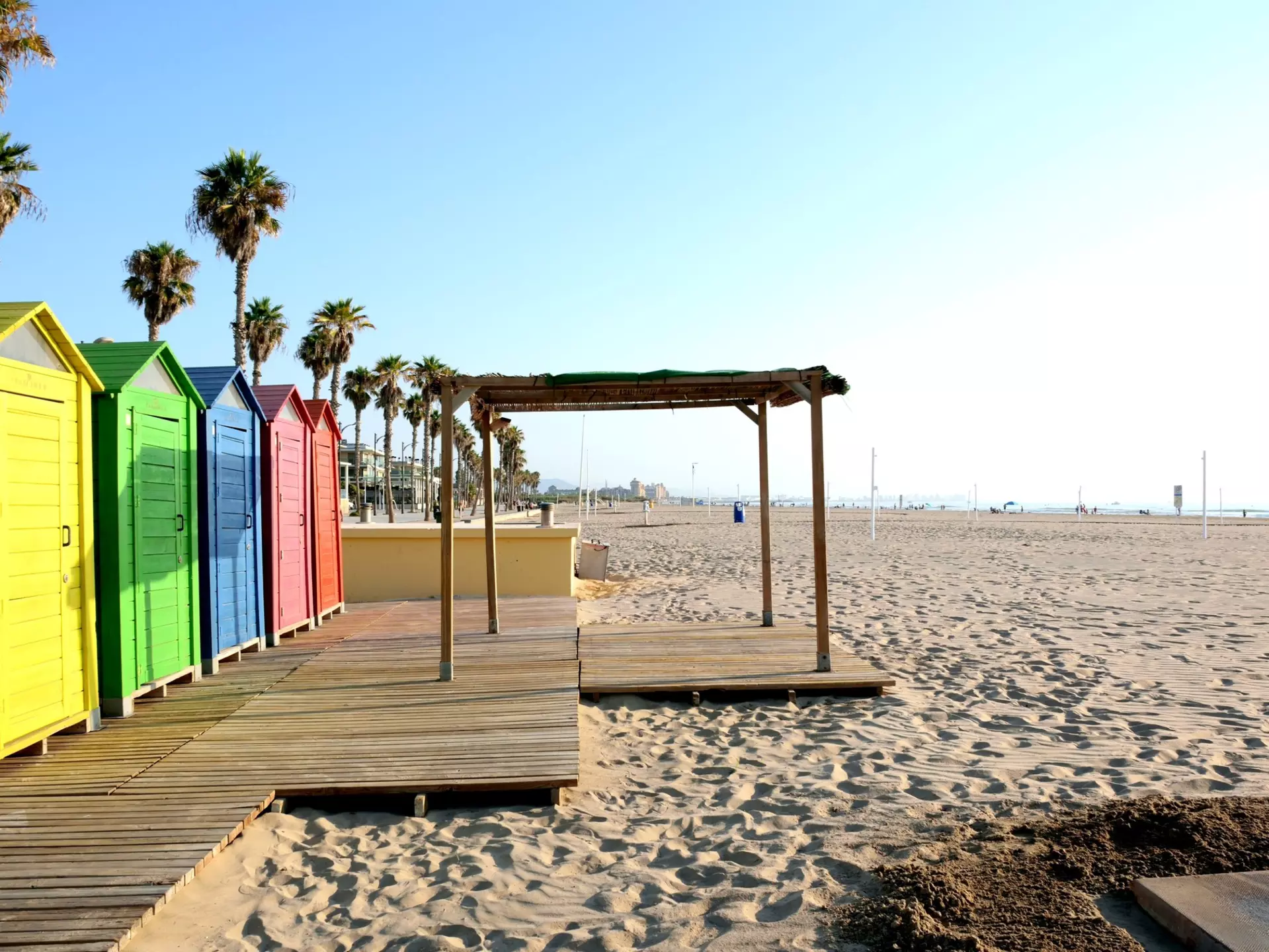 Brightly painted wooden cabins beside a sandy beach, lined with palm trees.
