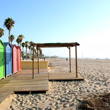 Brightly painted wooden cabins beside a sandy beach, lined with palm trees.