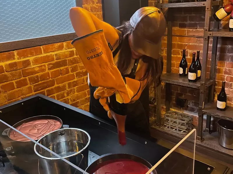 A person in protective clothing seals a wine bottle with warm wax