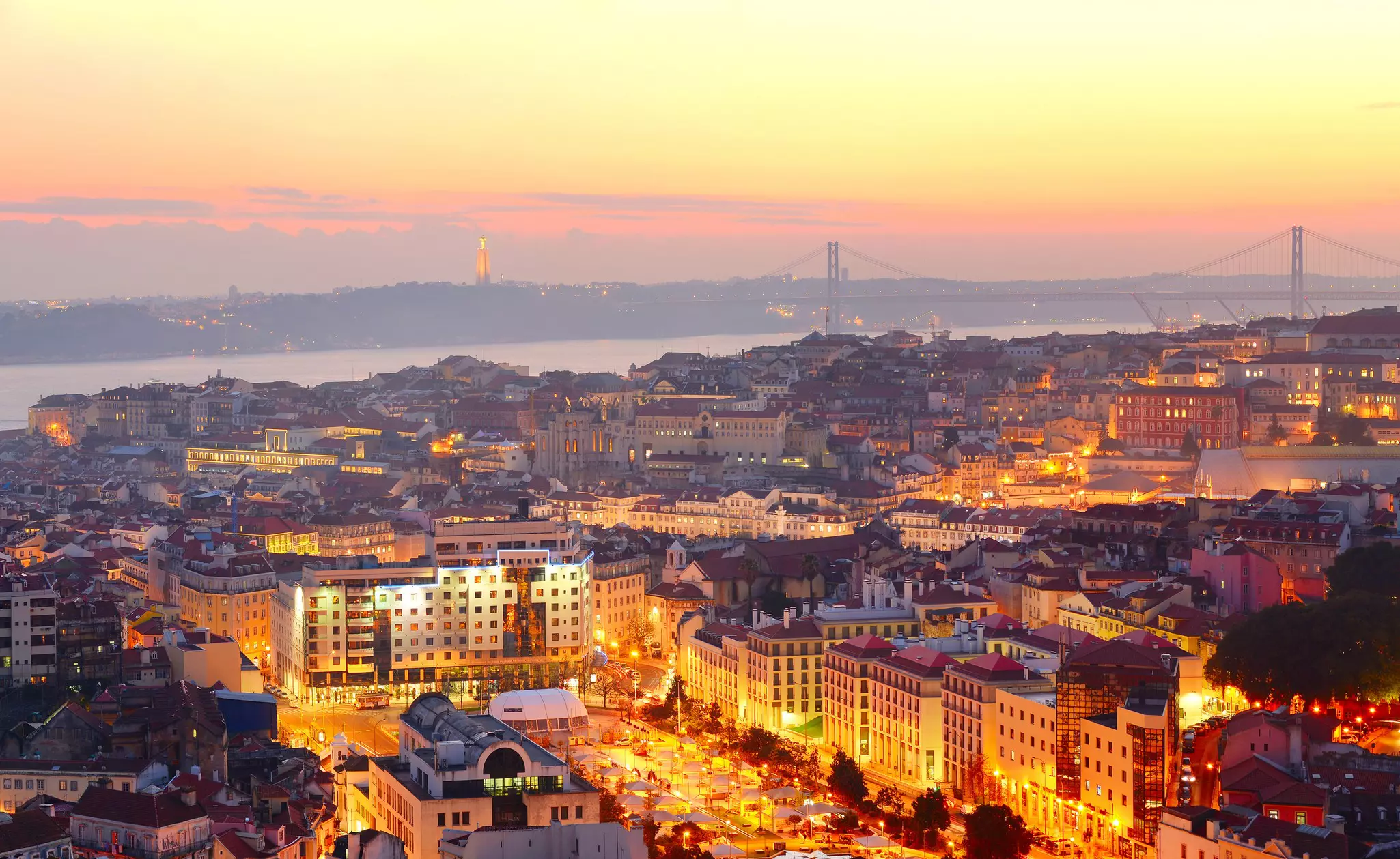 A riverside city skyline after sunset, with all the street lights and buildings lit up.