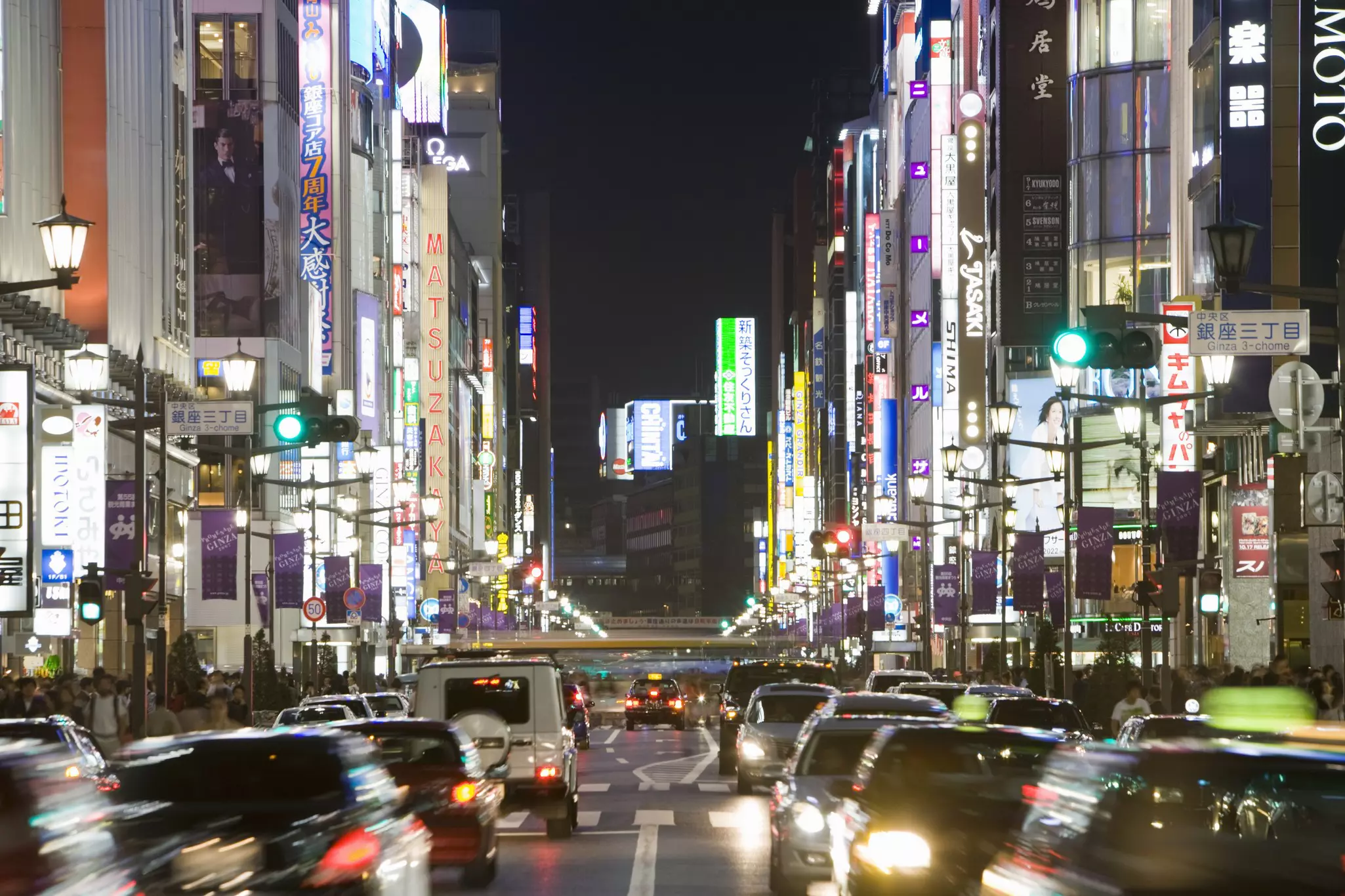 A street in Tokyo at night, very busy with traffic in motion, shops and signs are lit up