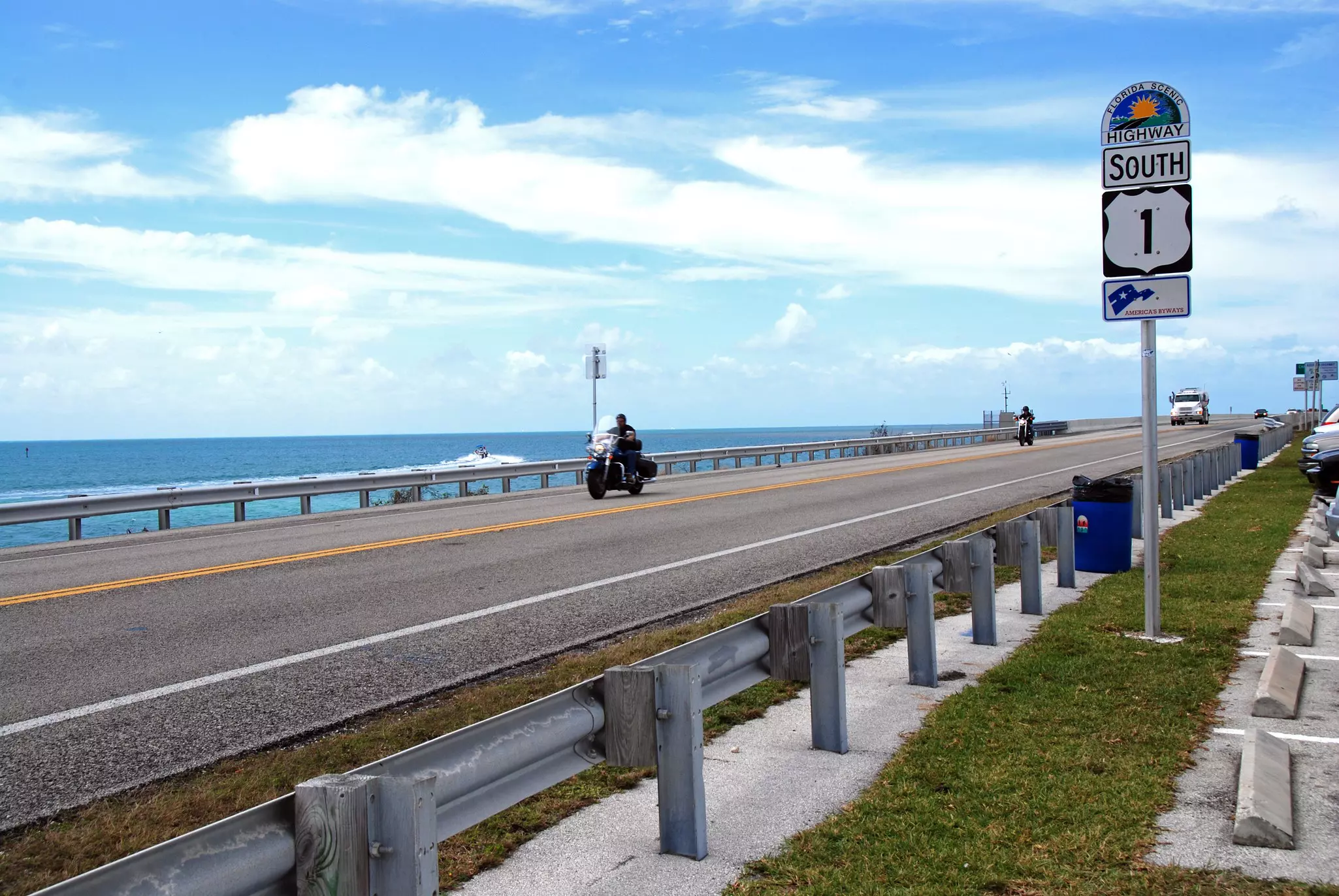 Two motorbikes and a truck drive along a coastal highway.
