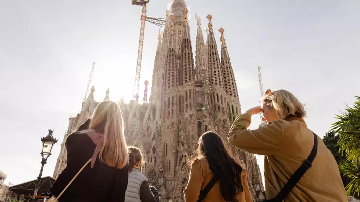 People look up to the spires of a cathedral with construction cranes.