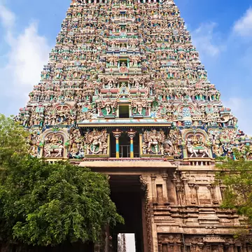 Towering temple gateway covered in brightly painted Hindu figures, with a dark stone entrance passage at its base