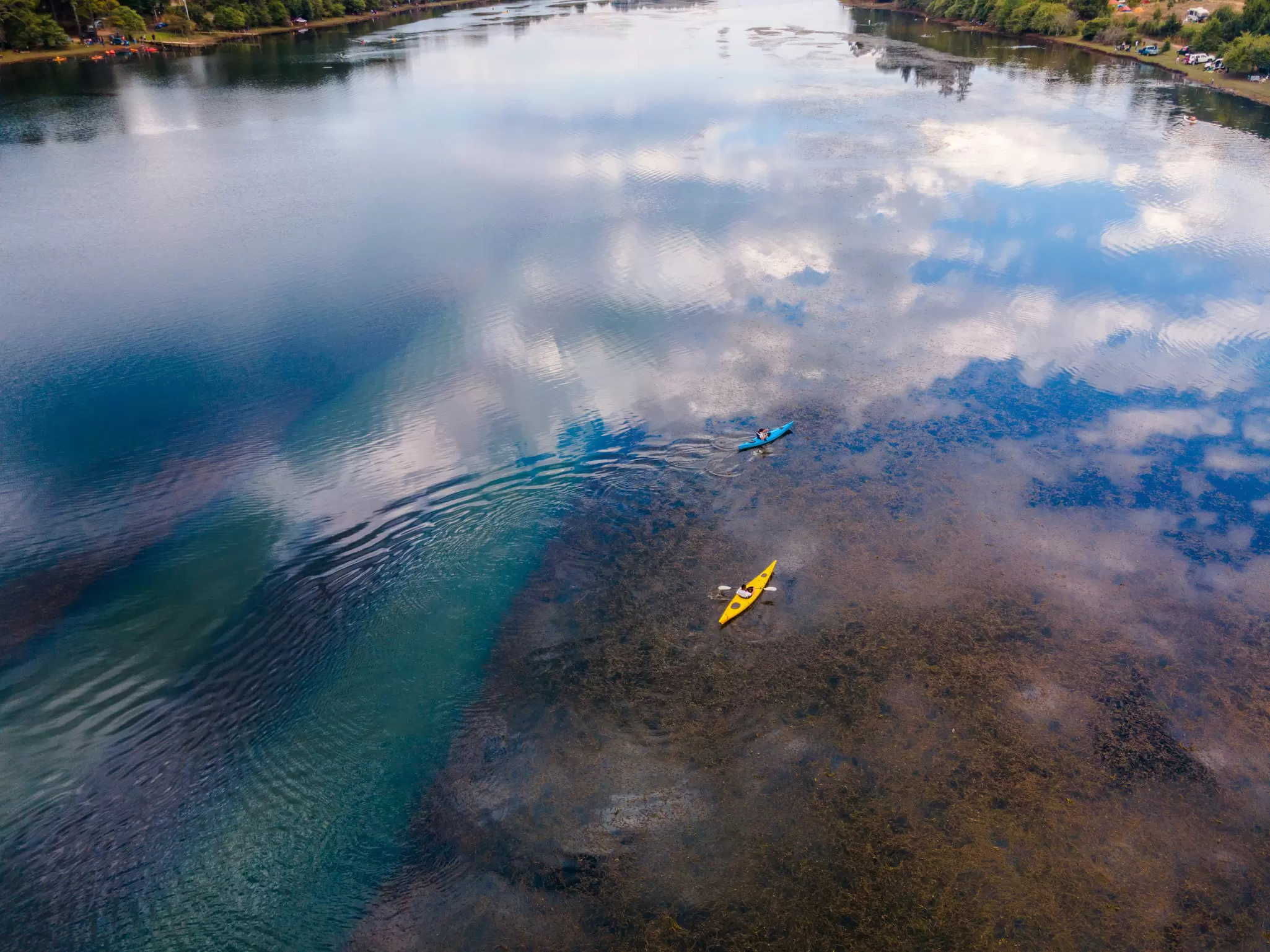 A yellow kayak and a blue kayak in a clear lake.