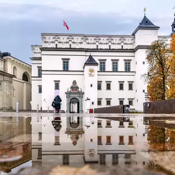 A white Renaissance palace and cathedral dome reflected in a rain-soaked square.