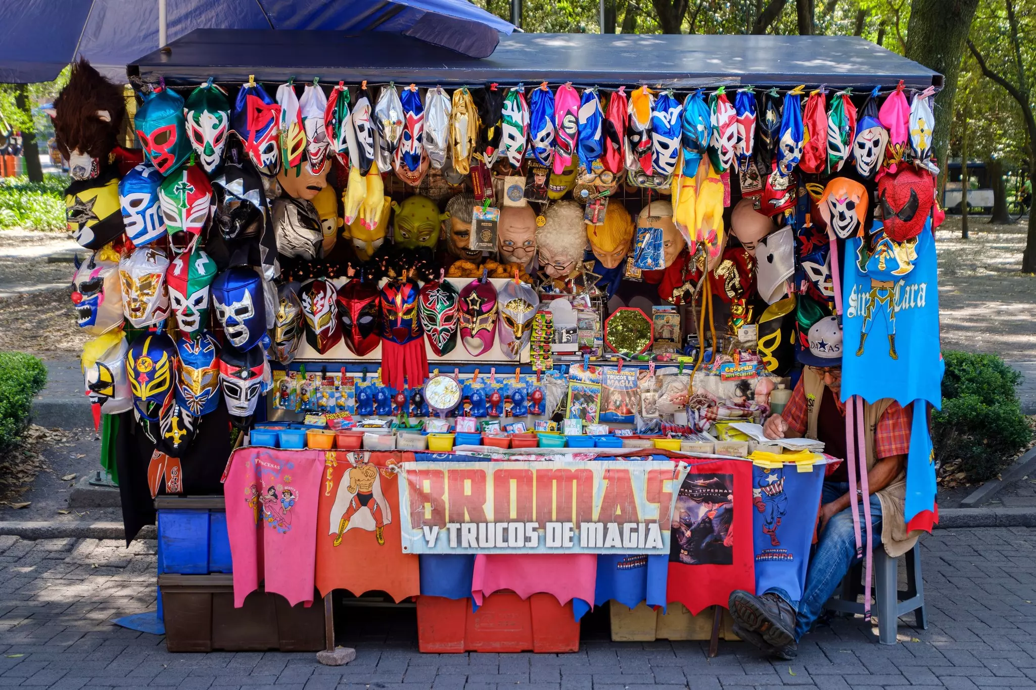 A vendor reads at his stand that sells various colorful lucha libre wrestling masks