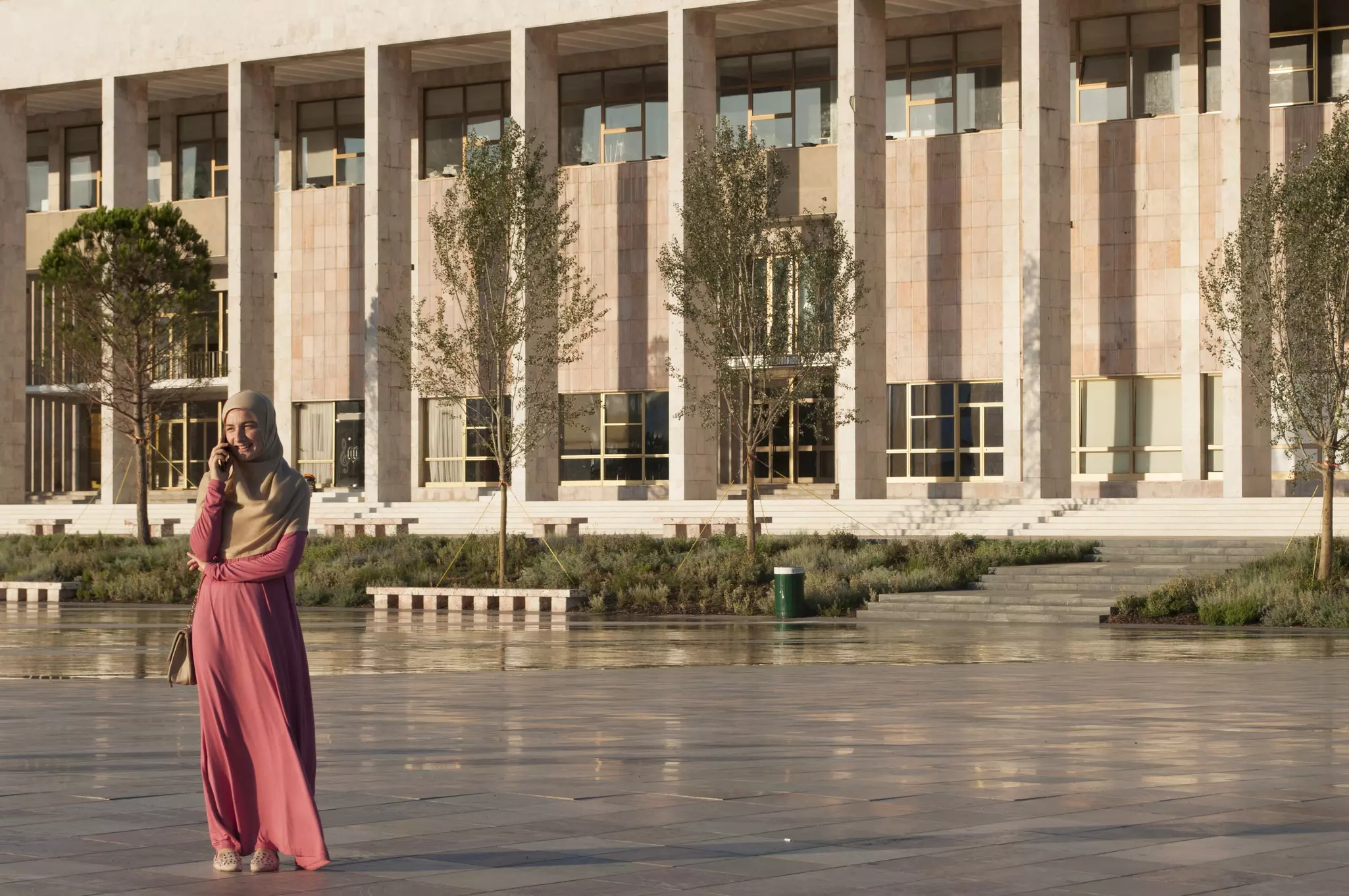 A woman smiles as she chats on her phone in a city square