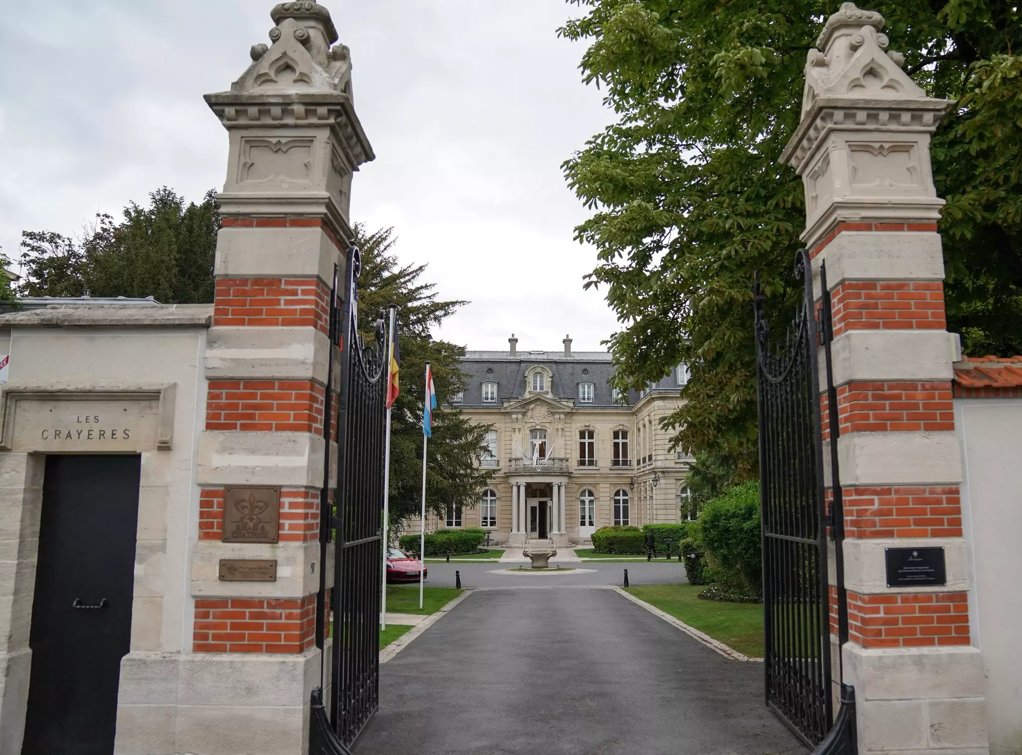 A gate leading to the entrance of a large ornate building with a circular drive in front of it