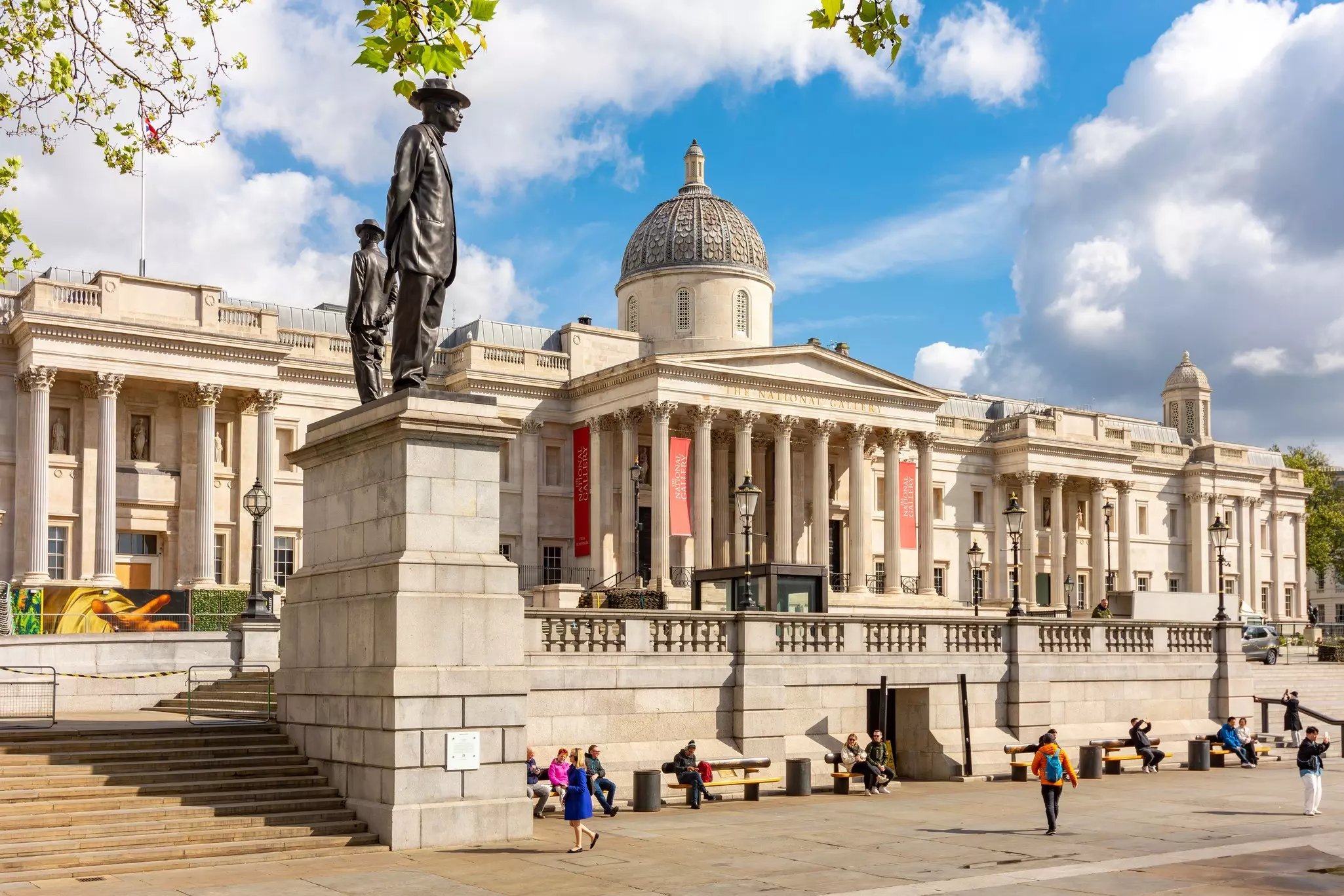People sit on benches in front of a large museum building with a dome and columns.