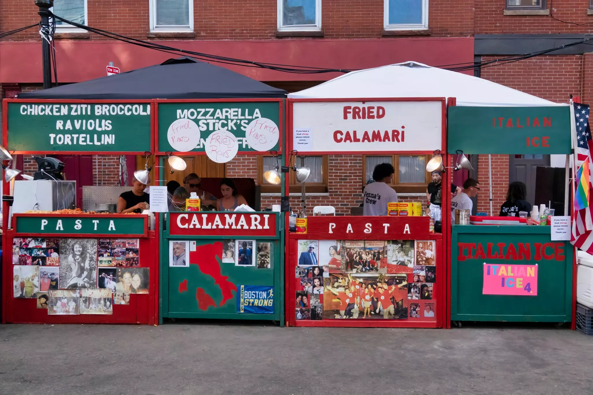 Wooden stands painted green and red with words like, fried calamari, mozzarella sticks and pasta. People are behind the stands