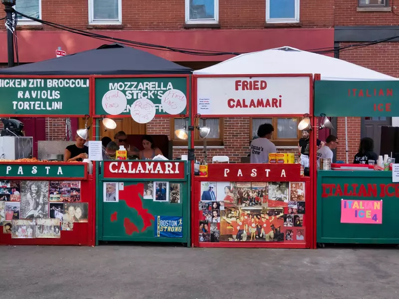 Wooden stands painted green and red with words like, fried calamari, mozzarella sticks and pasta. People are behind the stands