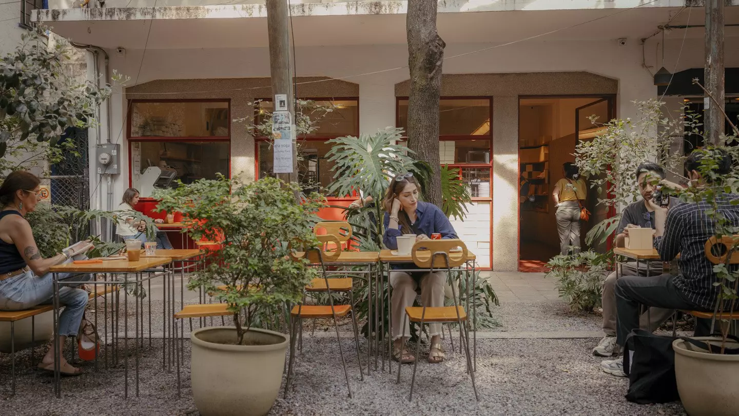 People sit at outdoor tables among plants in front of a bakery in Mexico City.