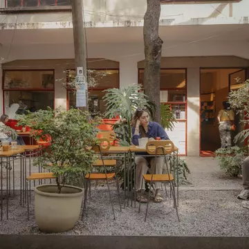 People sit at outdoor tables among plants in front of a bakery in Mexico City.
