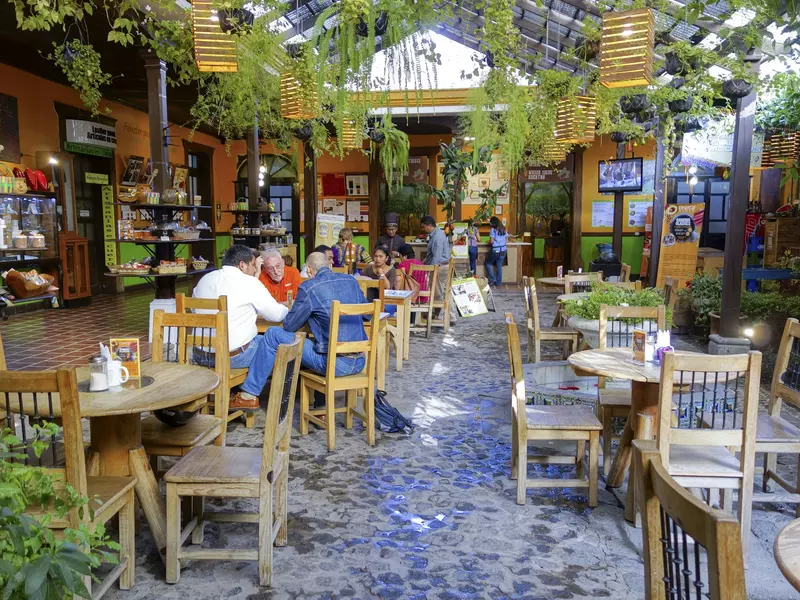 People sitting at outdoor cafe tables in a courtyard on a sunny day.