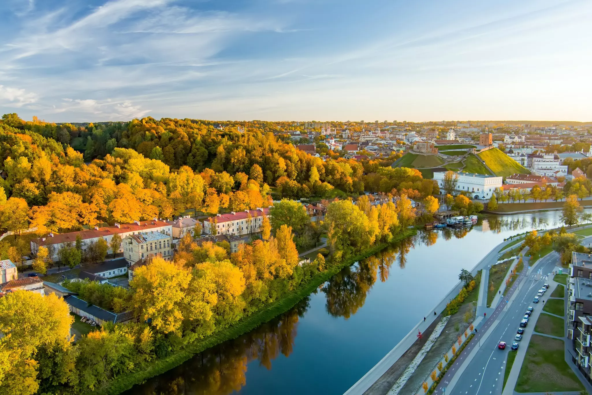 An aerial view of a low-rise city with red-roofed buildings surrounded by woodland covered in autumn foliage.