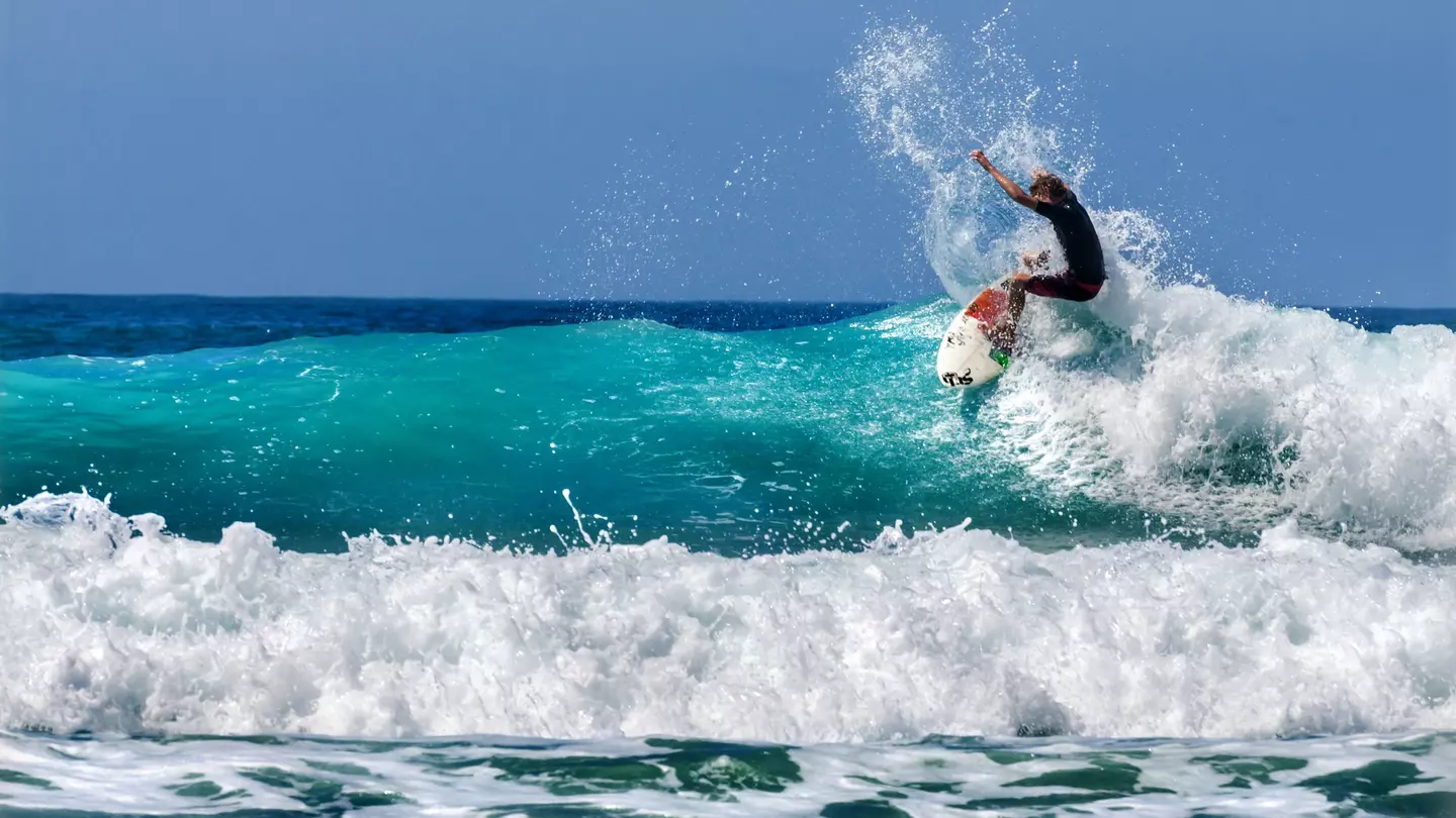 A surfer on a white and red board, riding a wave