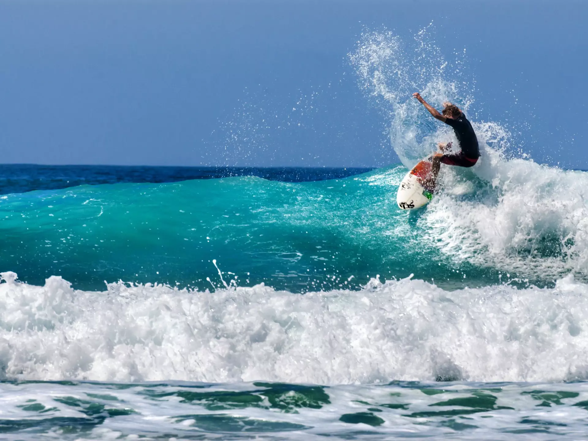 A surfer on a white and red board, riding a wave
