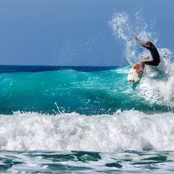 A surfer on a white and red board, riding a wave