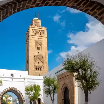 Sandstone minaret above white walls and arched gateways in Quartier Habous, Casablanca, seen through a brick arch