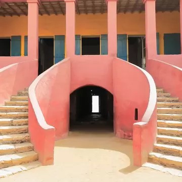 Pink plastered courtyard with two sweeping stone stairways around a dark arched corridor ending in a bright doorway