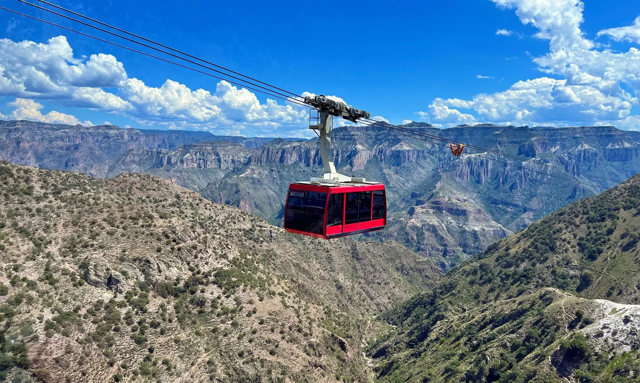 A red cable car travels up its track above a spectacular canyon.
