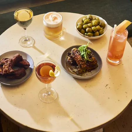An overhead view of a white table with drinks and small plates of food.