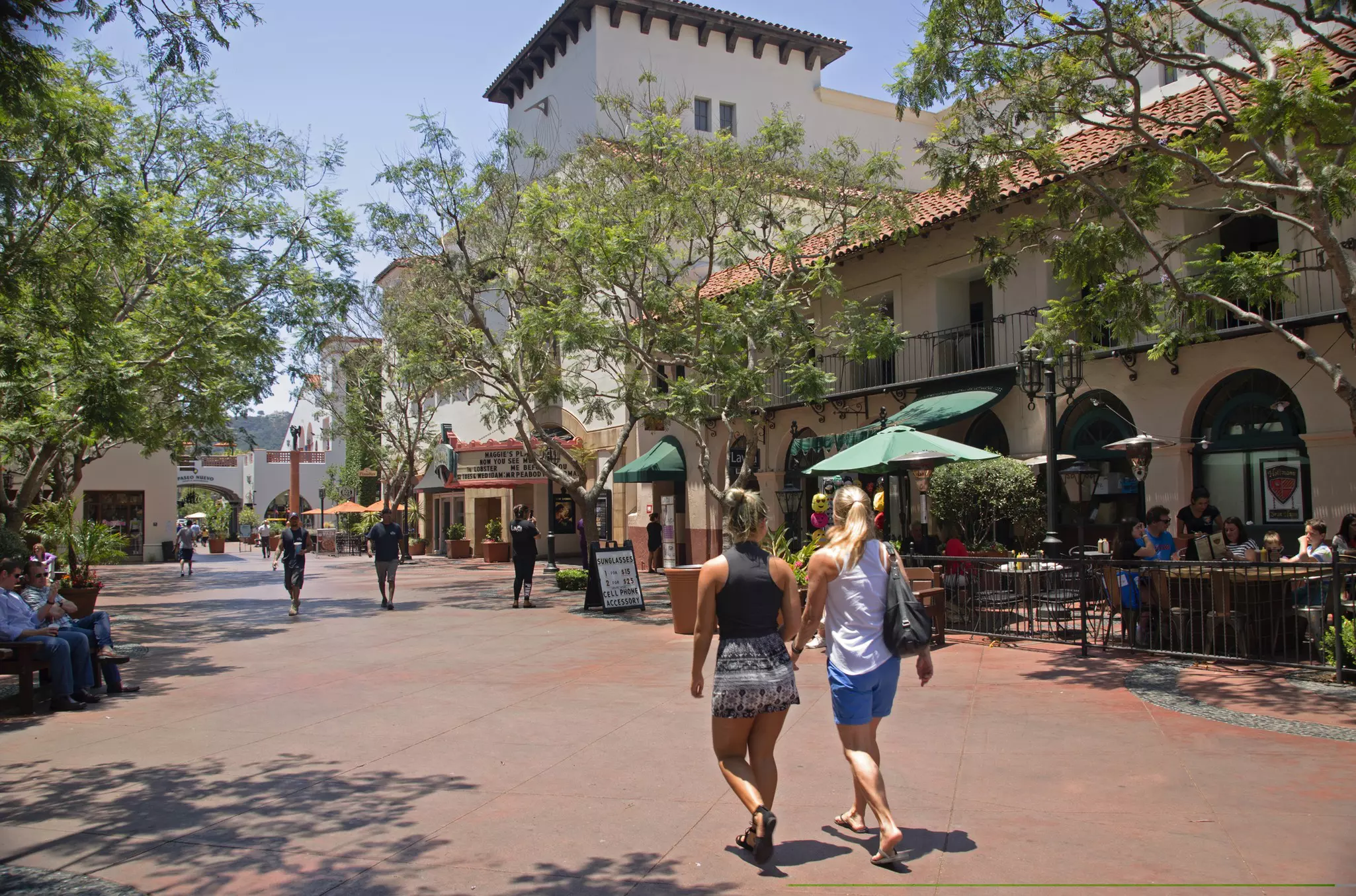 Two women walking on a plaza lined with restaurants and retailers