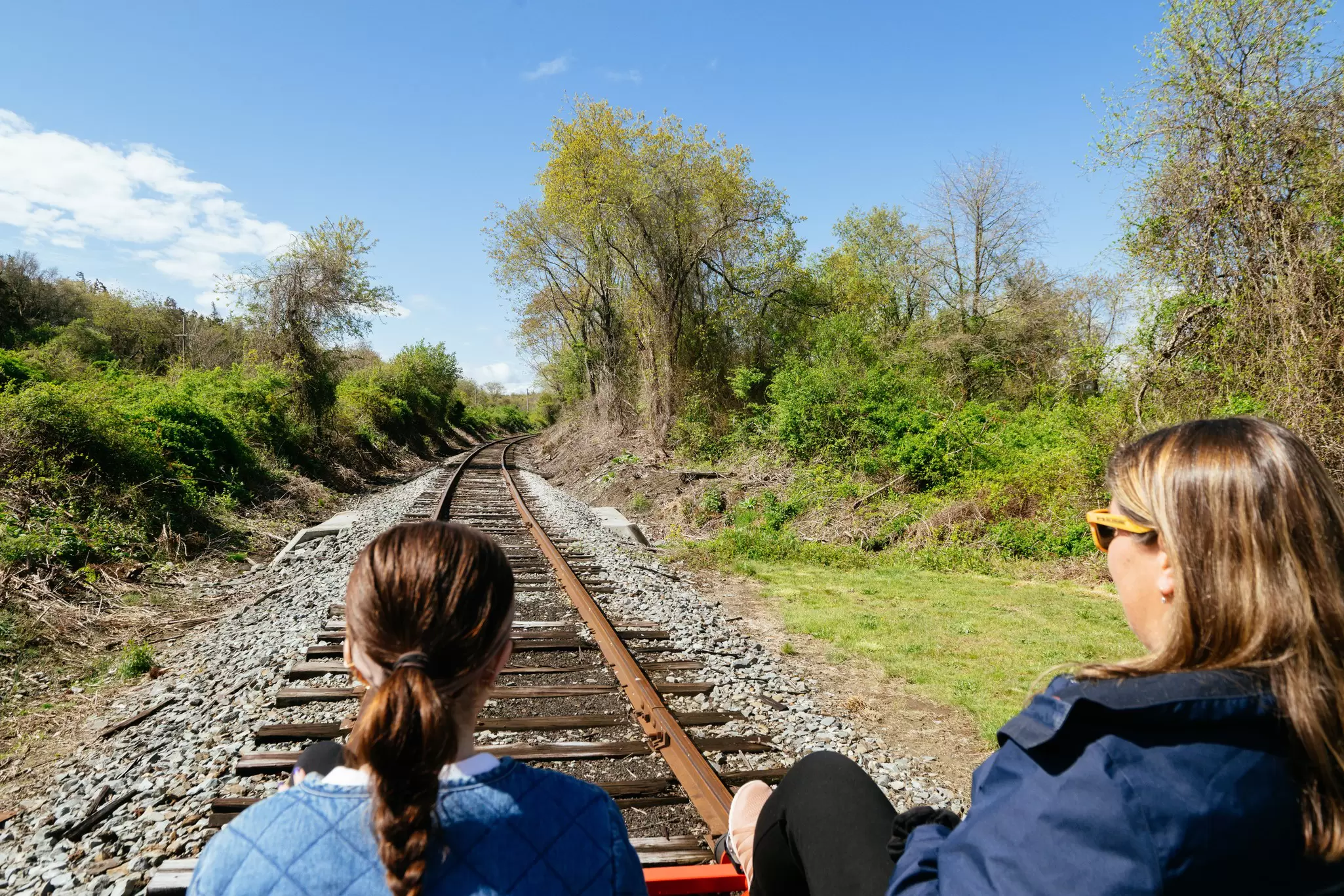View of two women on a cart on the Rail Explorers experience in Portsmouth, Rhode Island with train track ahead of them