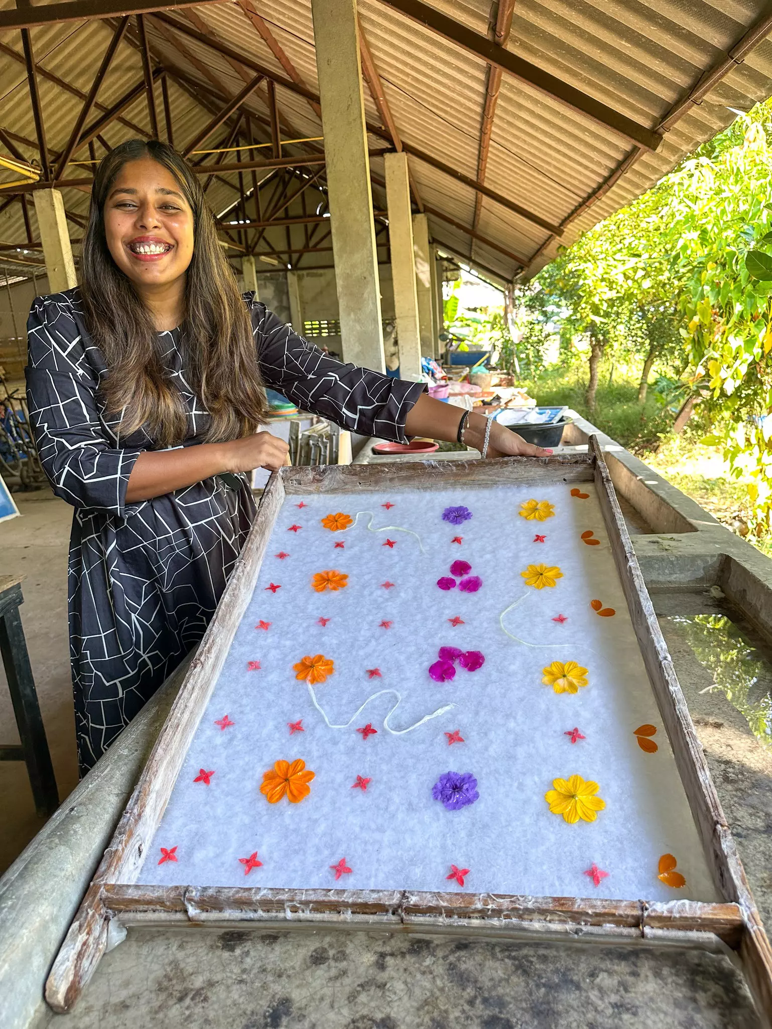 A woman smiles as she displays some traditional paper woven within a wooden rack and decorated with colorful flowers and petals.