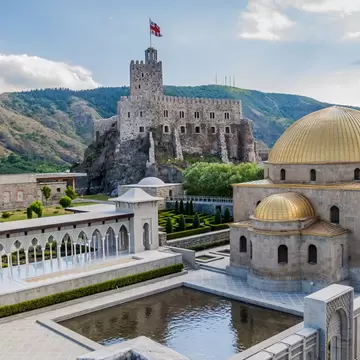 Rabati Castle, Akhaltsikhe: stone keep with Georgia's flag on a rock, gold-domed mosque, white arcade and reflecting pool