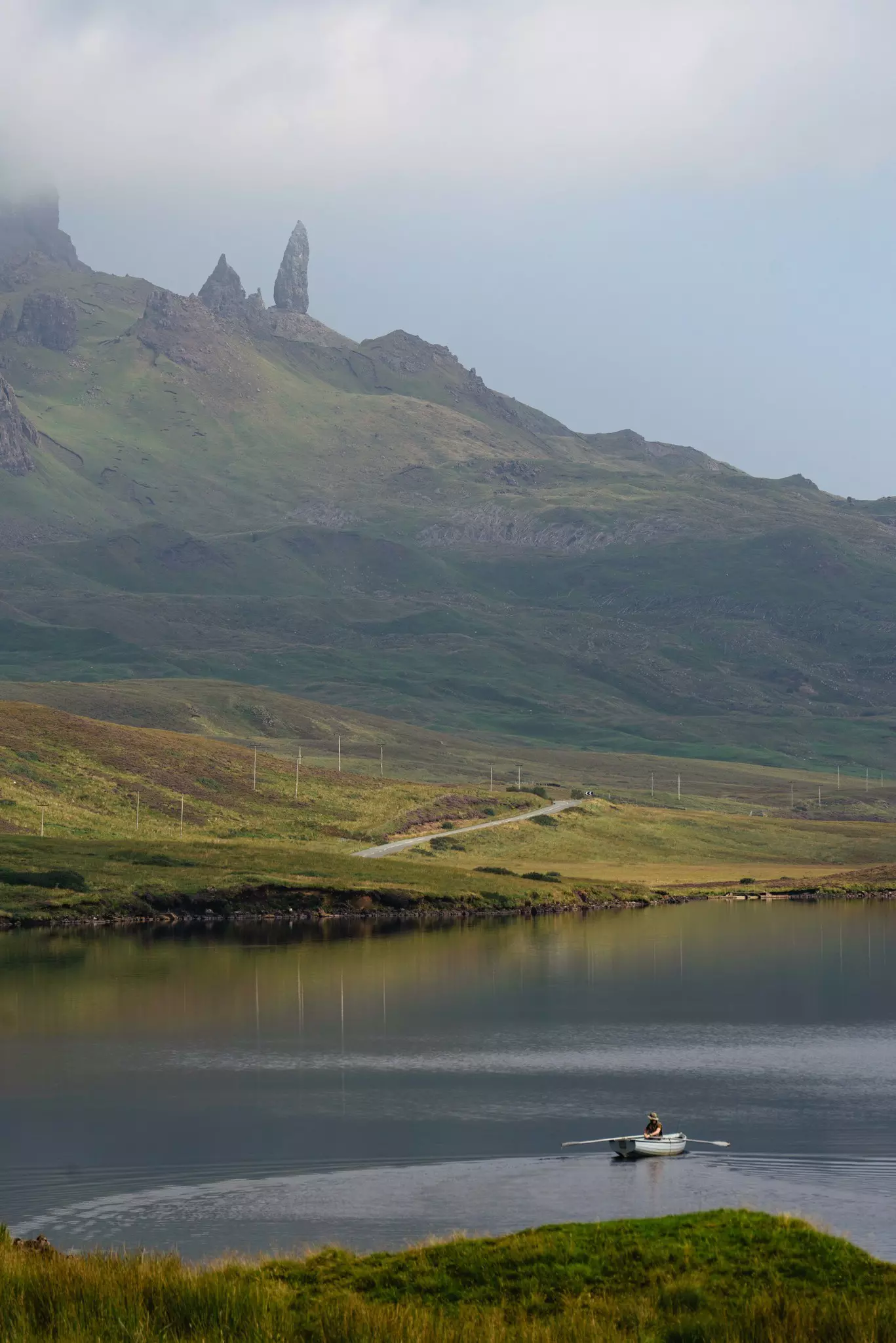 Man hiking in Scotland, Isle of Skye at the Old Man of Storr - Hiker climbing on rocks with the famous rock of the Isle of Skye on a cloudy  day