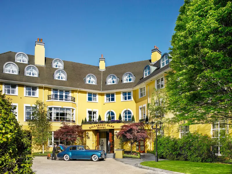 The exterior of a luxury hotel painted yellow. A green vintage car is parked at the entrance. 
