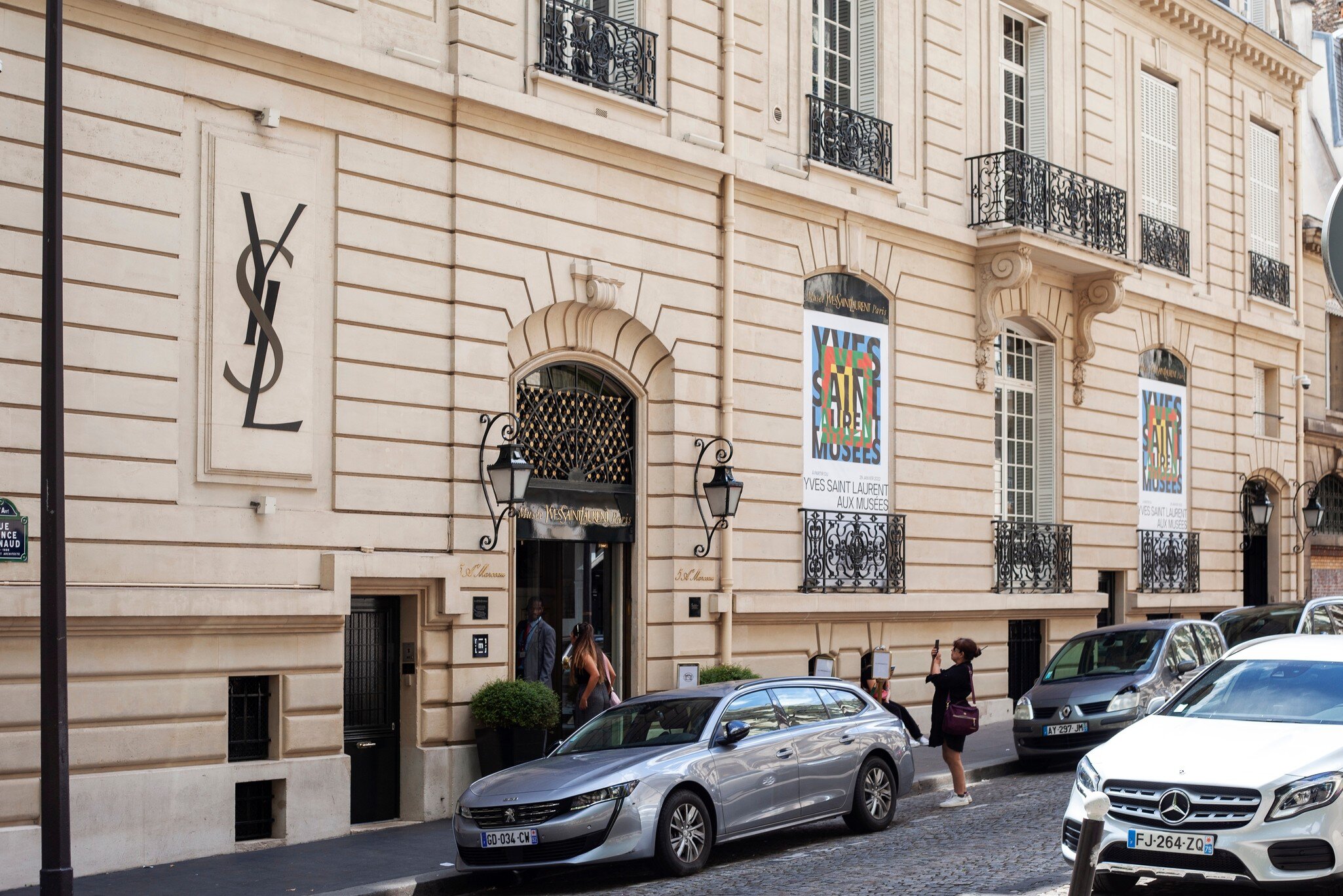 Exterior of the Yves Saint Laurent Museum in Paris (Musée Yves Saint Laurent Paris). Paris, France. Cars in foreground and woman taking photo in street.