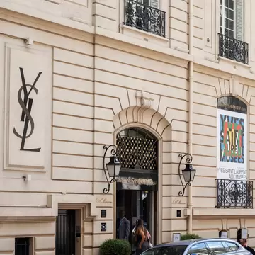 Exterior of the Yves Saint Laurent Museum in Paris (Musée Yves Saint Laurent Paris). Paris, France. Cars in foreground and woman taking photo in street.