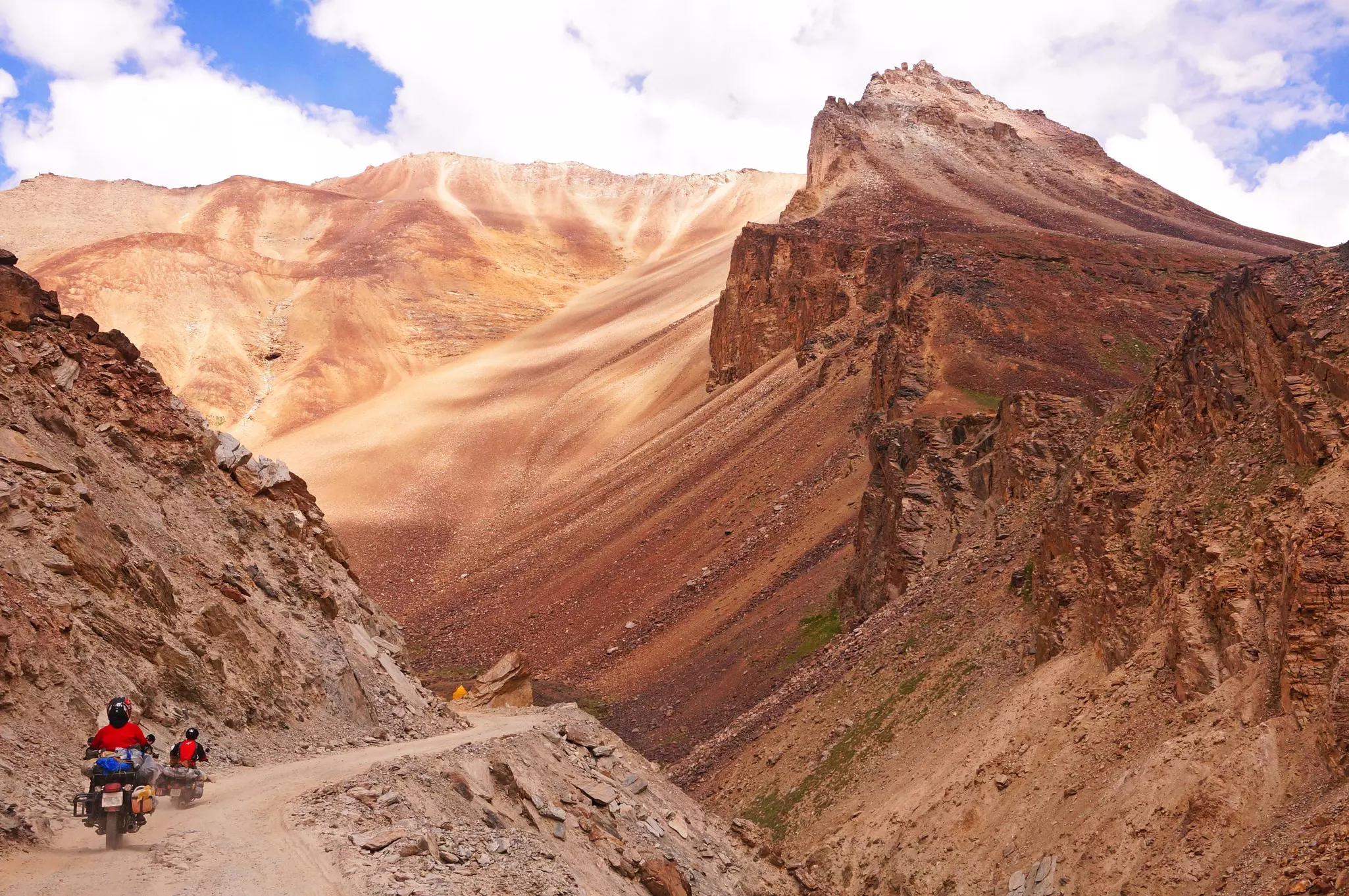 Two motorcyclists following a dirt road through dusty red mountains