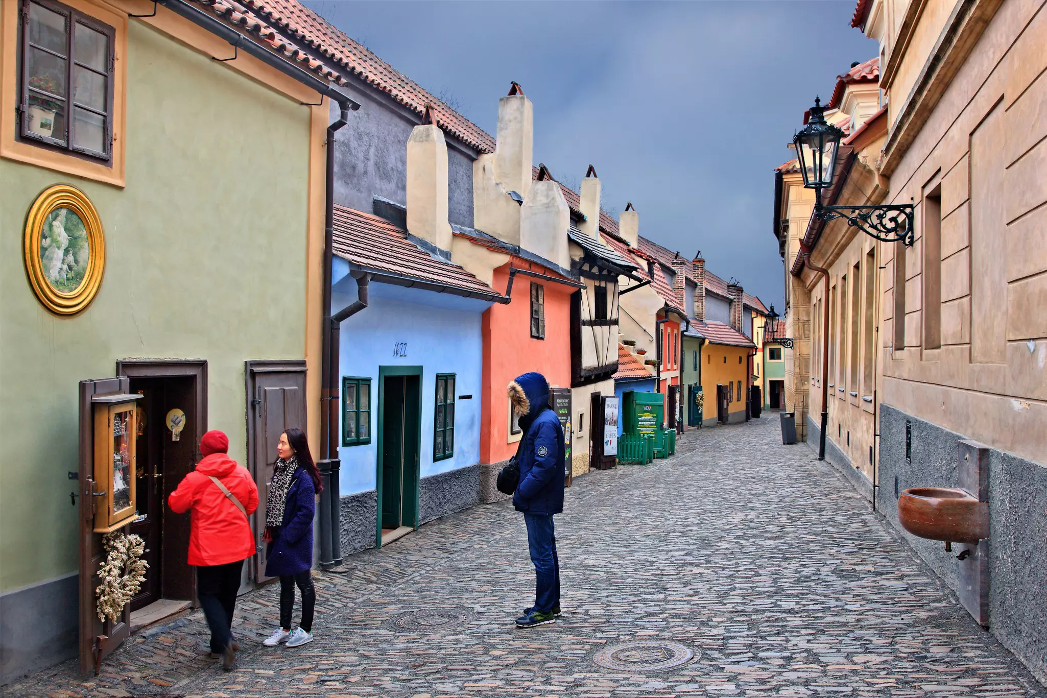 People stand in a narrow, historic cobblestone alley lined with small one-story houses