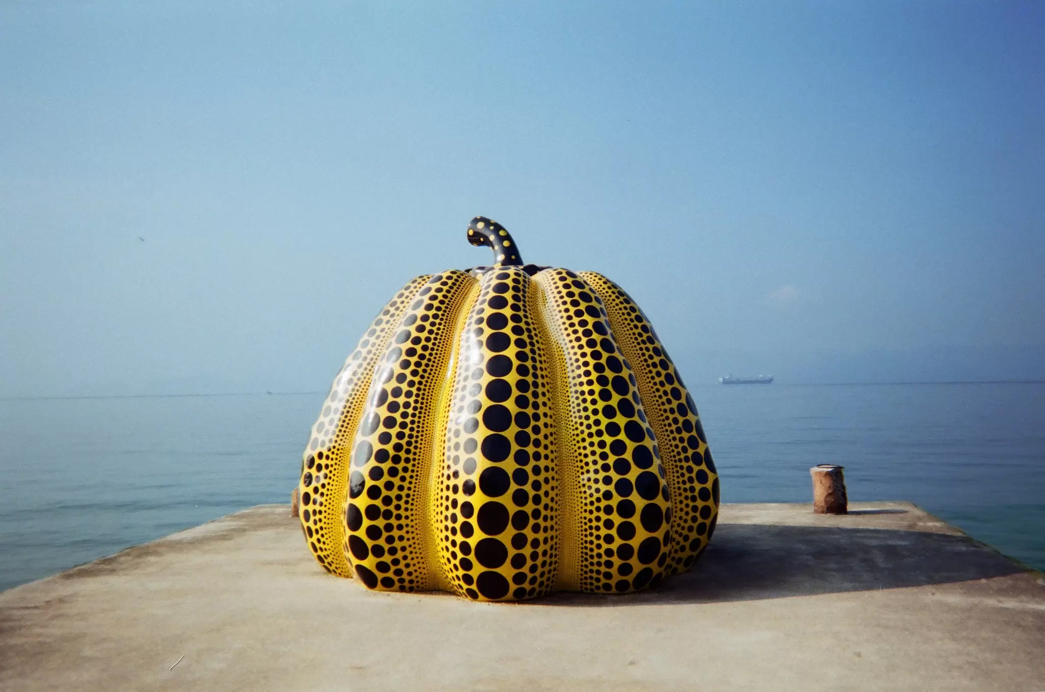 A large yellow pumpkin sculpture with black dots on a pier: "Pumpkin" by Yayoi Kusama.