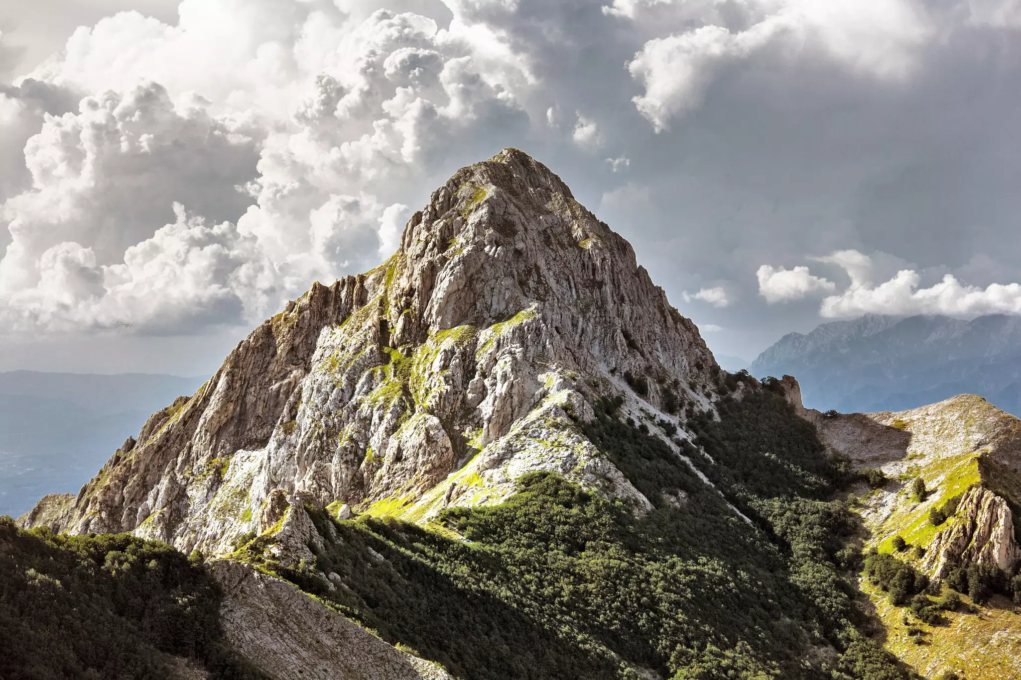 Wide shot of a rocky peak in the Apuan alps against a cloudy sky at sunset.