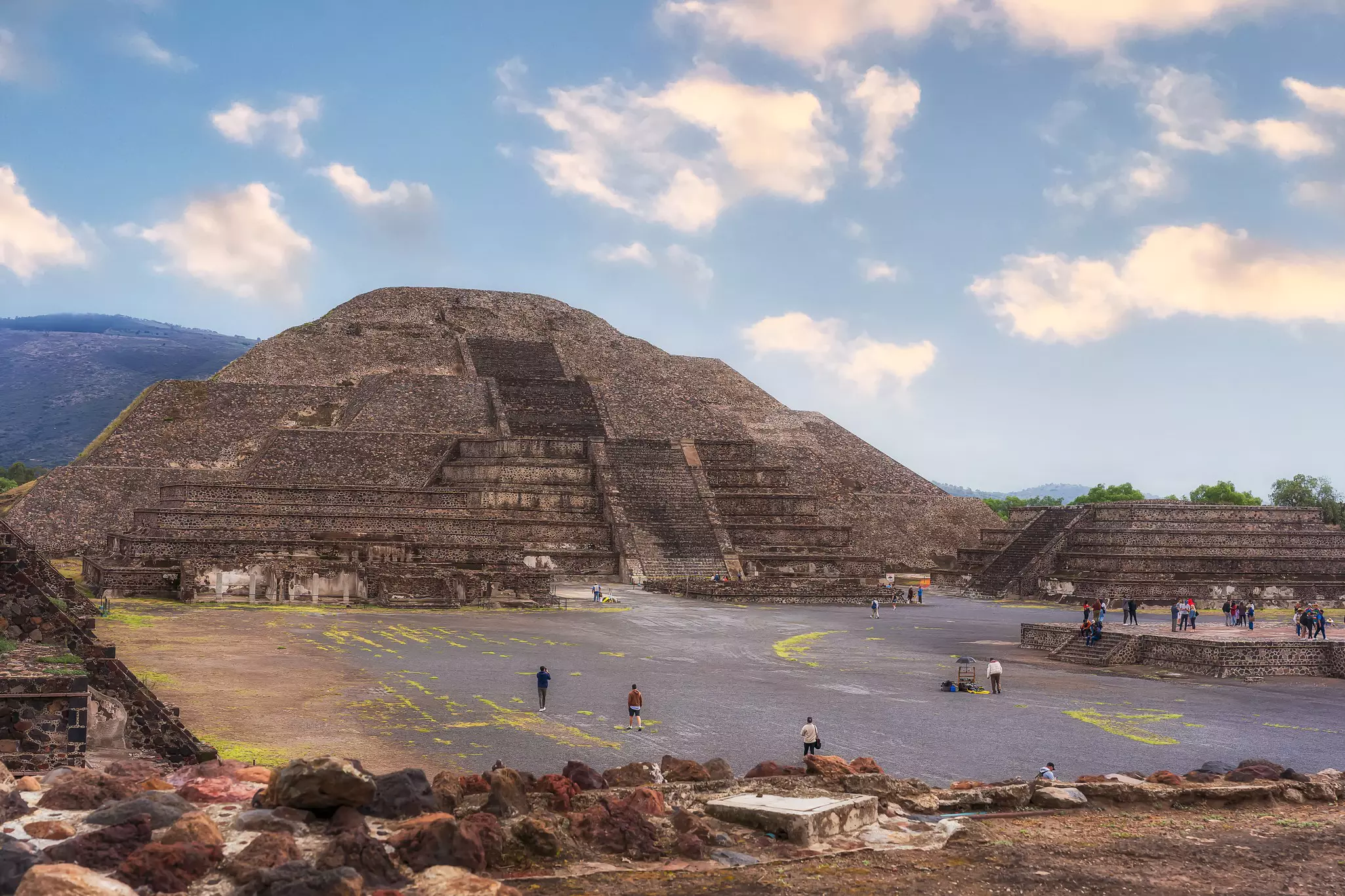 People cross a courtyard toward a massive stepped pyramid in Mexico.
