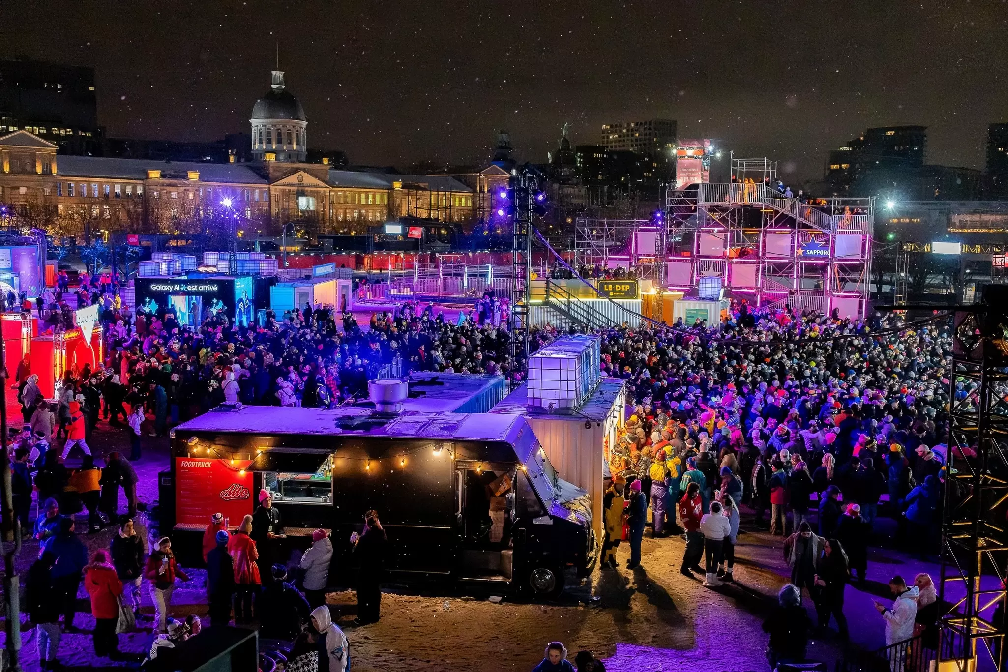 A wide view of an evening dance party in a city square, taking place as snow falls, Montréal, Québec, Canada